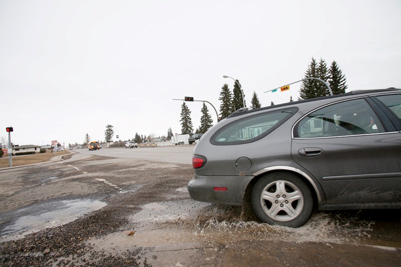 A vehicle drives through a pothole at the intersection of 46 Street and 52 Avenue on April 3.