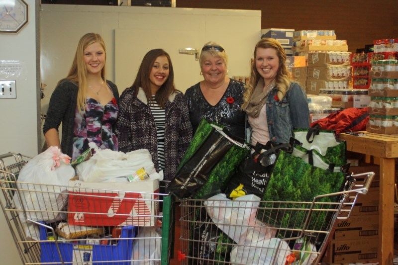 Olds High School leadership students Rebecca Vammen, Tirioin Goodinson and Keely Quilley (far right), present food students collected on Oct. 31 to Gayle Meier, a director