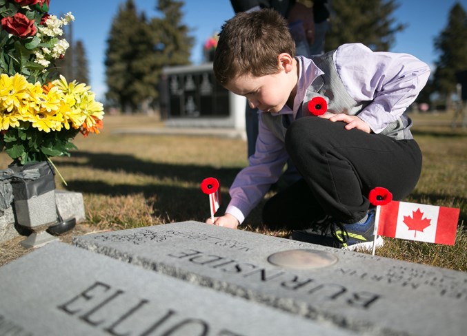 Robert Anderson places a flag at a gravestone at the cemetery in Olds.