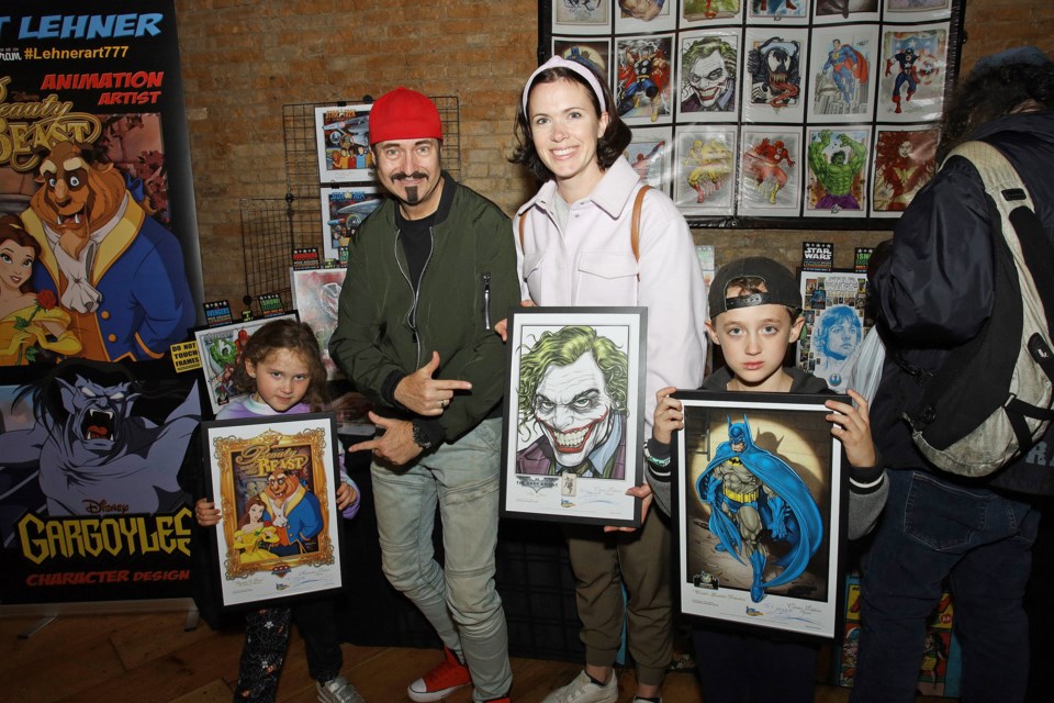 Emily Hill with her kids, Ellie and Bailey, hold up the Kurt Lehner prints she bought at the grand opening of Main Street Newmarket's Wayside Comics & Cocktails Saturday.