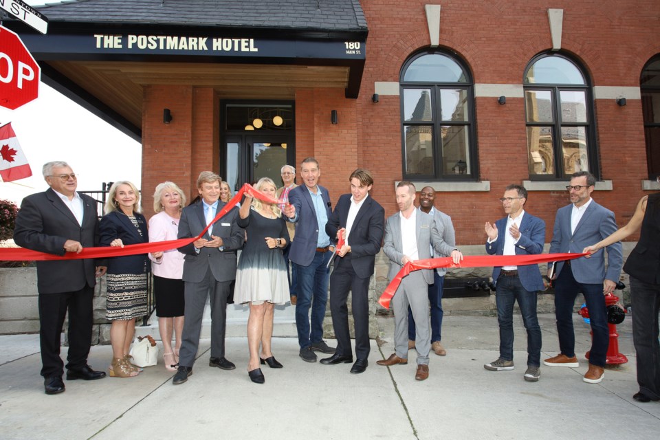 Dream Unlimited associate director Robb Dalgleish cuts the ribbon with Newmarket Mayor John Taylor at the entrance to the Postmark Hotel.  Also present are Newmarket-Aurora MPP Dawn Gallagher Murphy, Deputy Mayor Tom Vegh, and councillors Bob Kwapis, Grace Simon, Christina Bisanz, and Victor Woodhouse, Avi Wulfand, general manager of The Postmark Hotel,  Matt Cohen, Archive Hospitality executive vice-president, and Daniel Bernstein, president of Archive Hospitality Group.