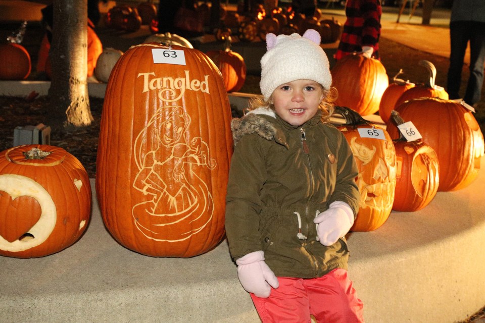 Adalyn Boorman measures up to one of the jack o' lanterns at  Newmarket's pumpkin parade last night at Riverwalk Commons. Greg King for NewmarketToday