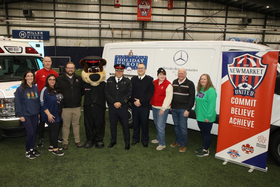 Newmarket Food Pantry 0perations manager Vanessa Gorgio, Newmarket Soccer Club GM Kevin Small, NSC president Petra Fera, Salvation Army Capt. Fred Reid, York Regional Police Const. Bucky, YRP Deputy Chief Alvaro Almeida, York Region Paramedic Services Acting Chief Jeremy Watts, Salvation Army community relations representative Angela Covert, Newmarket-Aurora MP Tony Van Bynen, and Megan Stoddard gather for the launch of YRP's 28th annual Holiday Heroes toy and food drive at Newmarket Soccer Club Nov. 16.