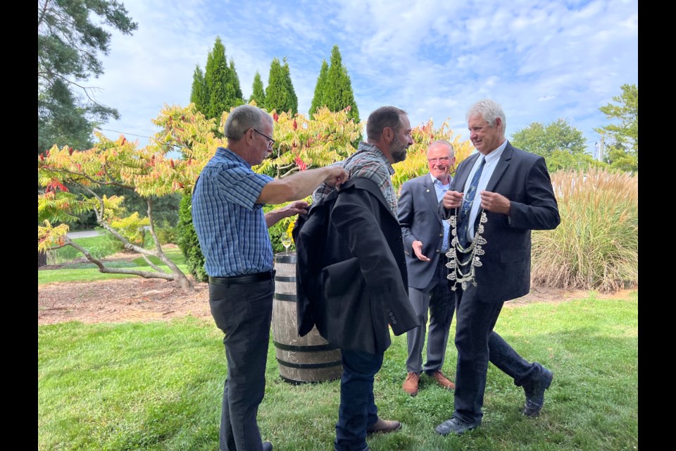 Ray Duc helps Jeff Duc into the 2024 Grape King jacket while outgoing Grape King, Erwin Wiens, approaches with the ceremonial collar.