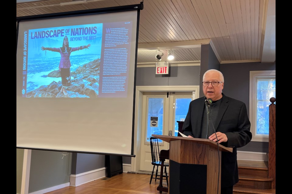  Co-editor and contributor, Tim Johnson, stands beside an image of the cover jacket depicting award-winning artist, dancer, choreographer and chancellor of McMaster University, Santee Smith.