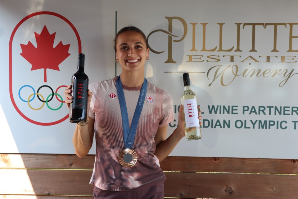 Kylie Masse, Olympic bronze medal around her neck, holds up the red and white wine that each has her name on the label. 