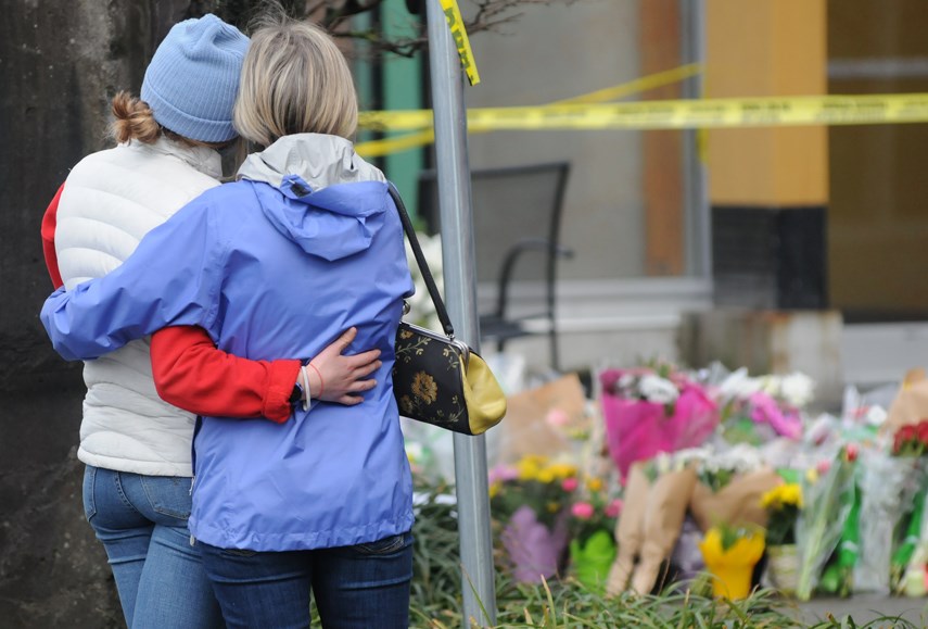 Two women pause at a growing memorial at the Lynn Valley library Sunday, March 28, one day after a man killed one person and injured six others in a stabbing attack in 2021.