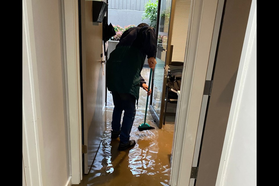 A colleague sweeps out water at the West Vancouver HearingLife Canada location on Bellevue Avenue after the atmospheric river that swept through Oct. 19 to 21. 