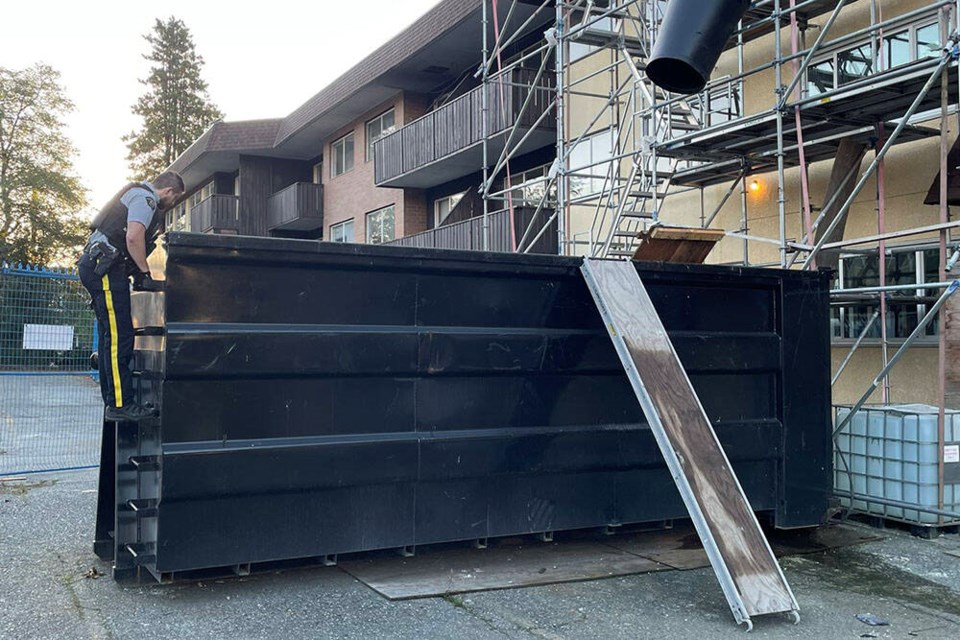 A North Vancouver RCMP member helps craft an escape route for a raccoon family stuck in a dumpster Sept. 29. | North Vancouver RCMP 