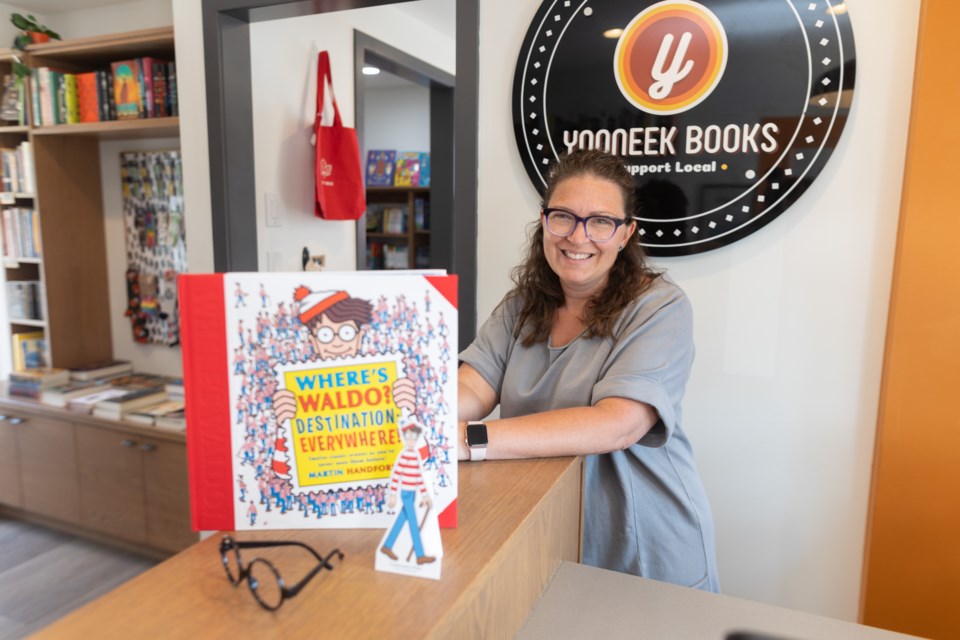 Yooneek Books co-owner Rae-Lynne Byerley poses with various material from the 'Where's Waldo in Okotoks!' event in her shop on July 5. Through the month of July, a cardboard cutout of Waldo will be hiding in 22 businesses around town for customers to seek out.