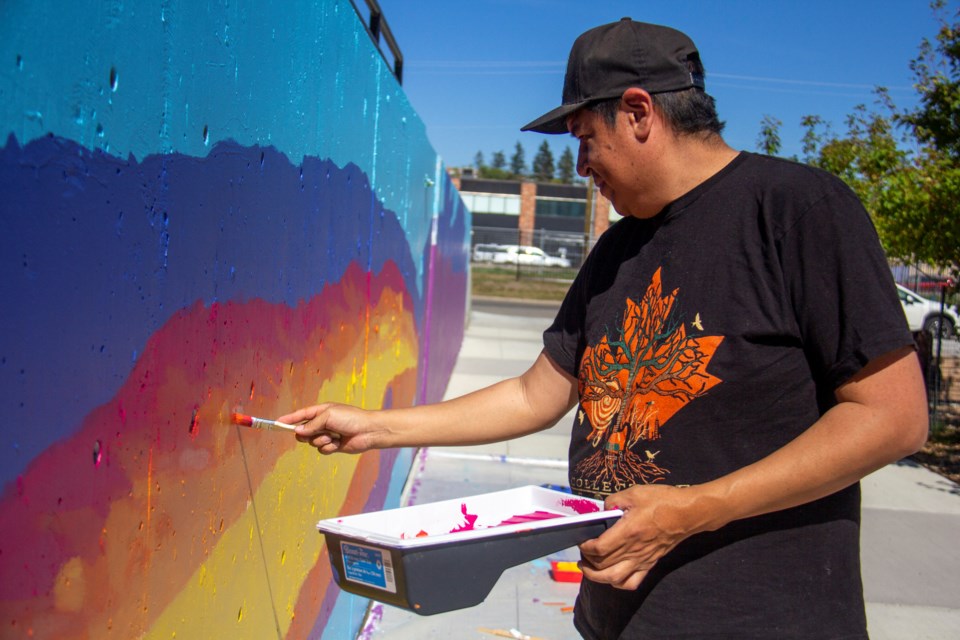 Stoney Nakoda artist Gordon Wesley, pictured on Sept. 5, is working on a mural at the Arts & Learning Campus Plaza depicting the Sheep River before colonization, which is set to be completed before the end of the month.