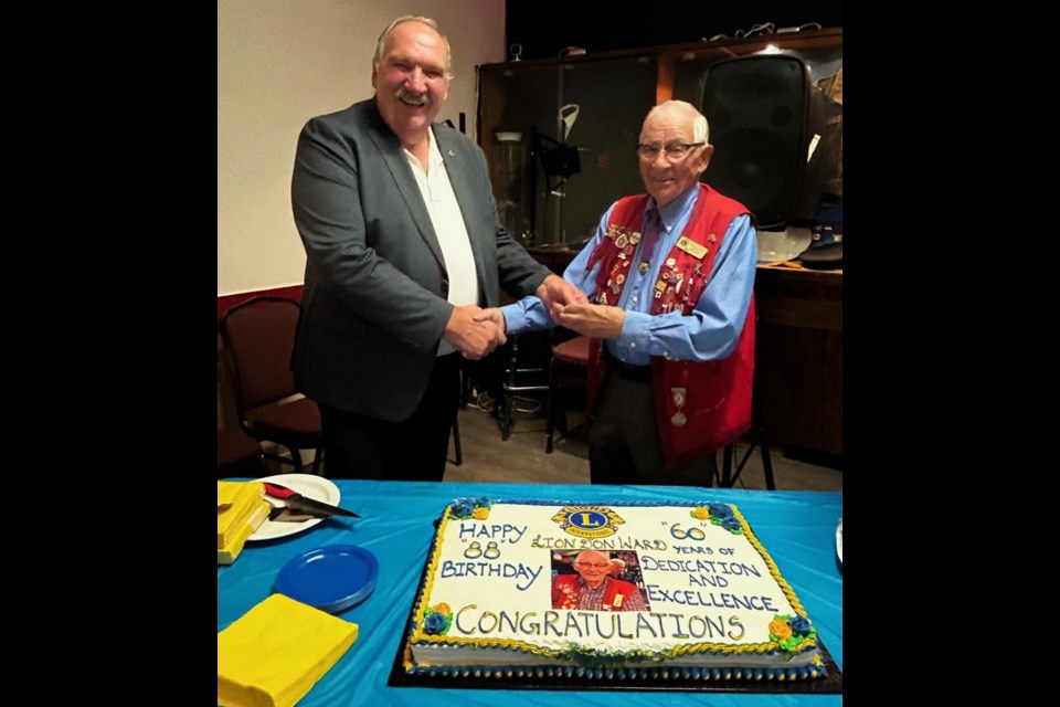 Foothills Lions Club president Garry Raab pressing Lion Don Ward with his 60-year chevron. 