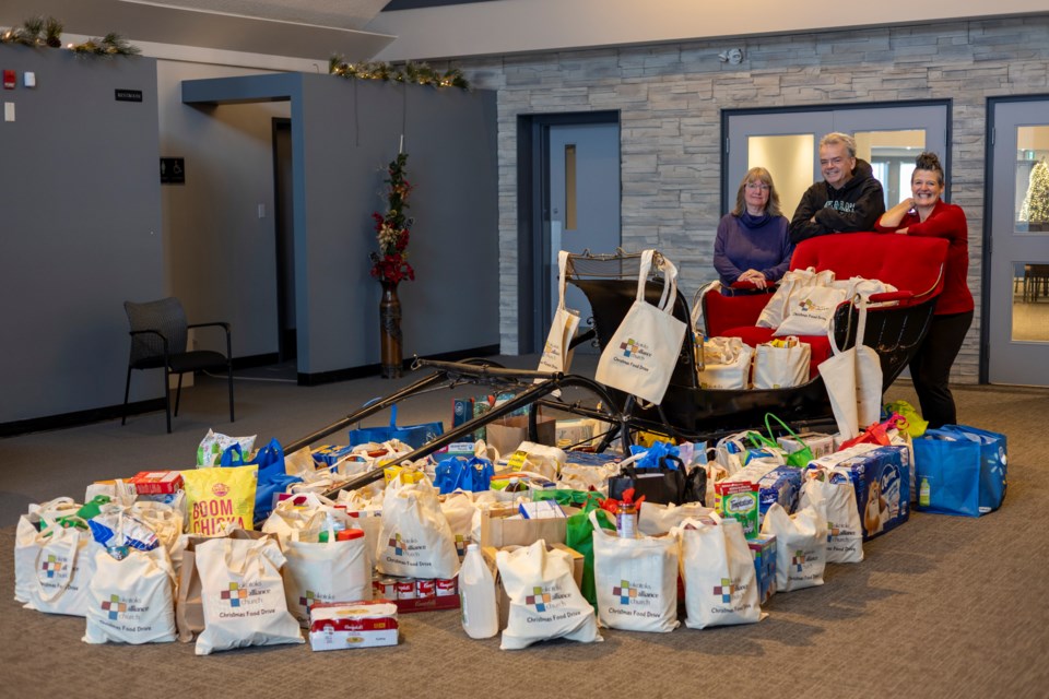 Okotoks Alliance Church administrator Valerie Climie (left), lead pastor Ian Trigg and associate pastor Gay Spence pose for a photo with the church's sleigh full of food on Dec. 18, before delivering their donation of 1,356 pounds of food to the Okotoks Food Bank the next day.