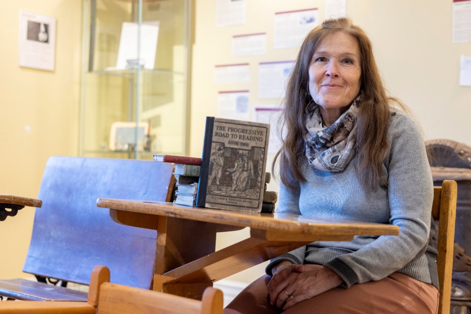 Kathy Coutts sits in a desk reminiscent of those used in one-room schools, complete with an inkwell, in the Okotoks Museum and Archives' one-room schools exhibit.