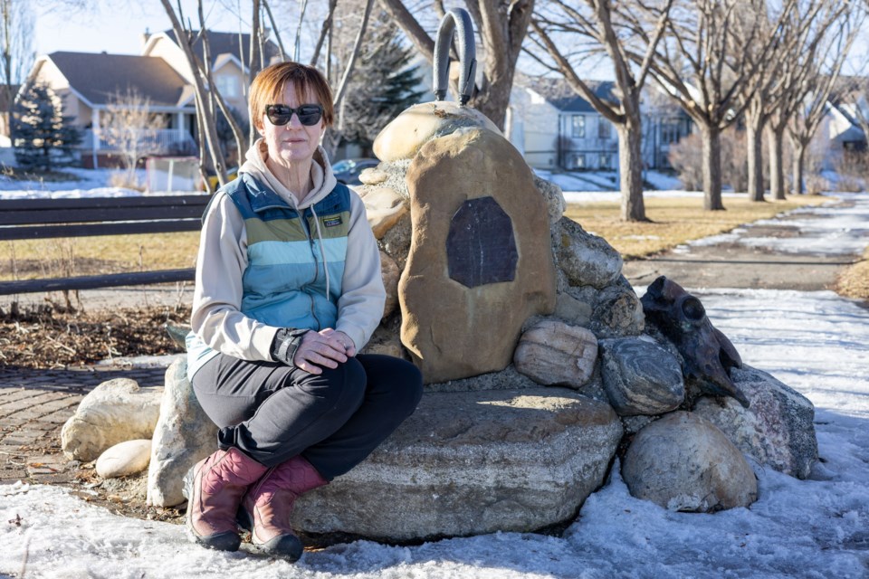 Concerned Okotoks resident Sheila Hughes poses for a photo with Rocky Barstad's statue in Westridge Close Park, pictured after the disappearance of a steer skull that was located on top of it, on Feb. 25. 