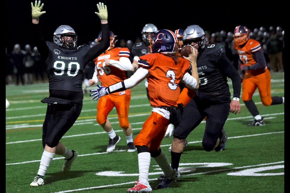 Holy Trinity Academy Knights defensive lineman Britton Burnand (90) rush end Ben Haden (6) put the pressure on W.H. Croxford Cavaliers quarterback Marshall Diggens during provincial playoff football action at Cochrane High School on Nov. 1. HTA won by a 47-0 score to advance to the provincial quarter-final.