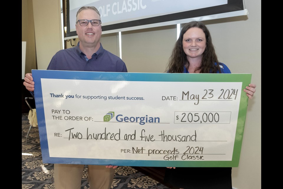Kevin Weaver, president and CEO of Georgian College, accepts a cheque from Georgian graduate and Golf Classic committee co-chair Addison Wallwin at the end of the event.