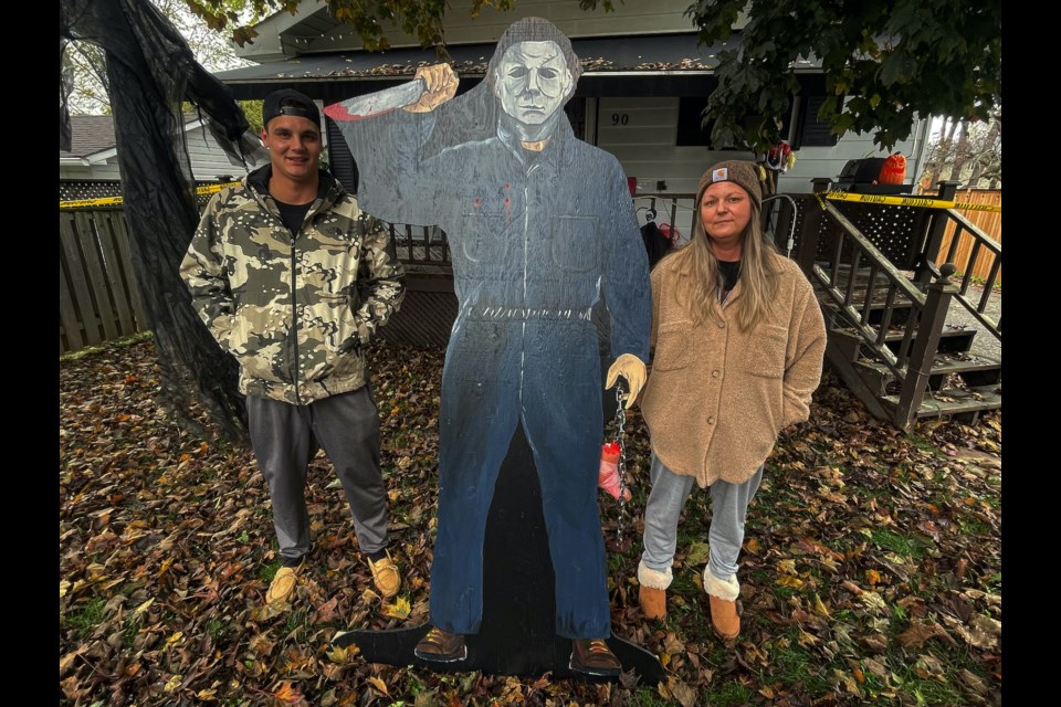 Lisa Petrie and her son, Taylor, proudly stand with the seven-foot wooden Michael Myers cut-out prop that was hand-crafted and painted by Bill and Lindsay Griffin, who stepped up to donate it to the family after their decorations were stolen.