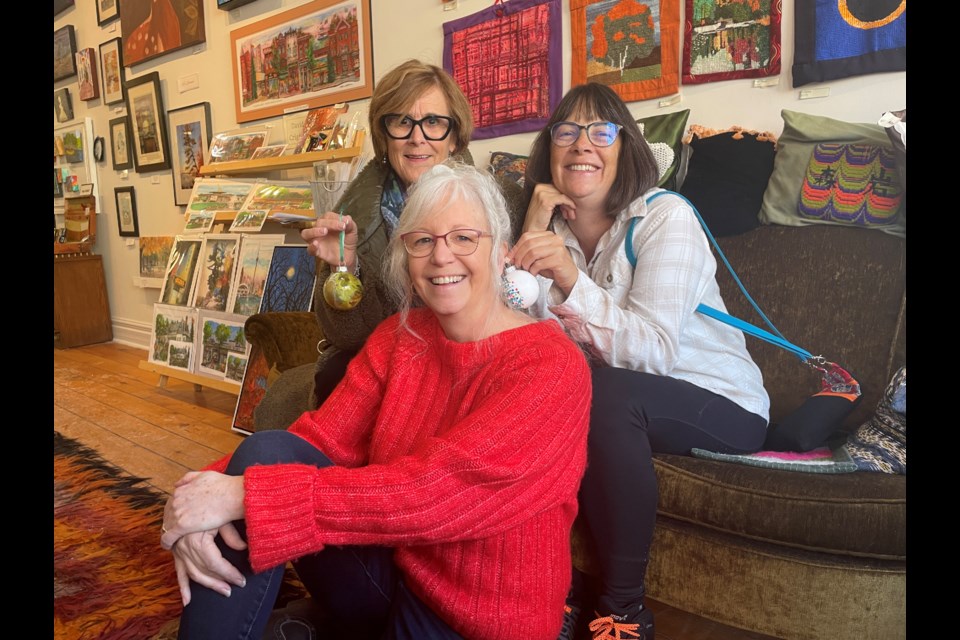 Merry Streets Alive oganizer Leslie Fournier sits in front of Marci Csumrik, left, and Anna Proctor as they pose with their chosen ornaments at Saturday's event in downtown Orillia.