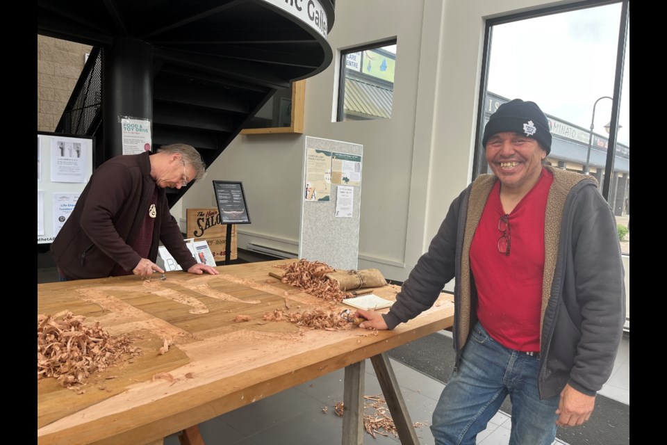 FAMILY HISTORY: Carver and qathet resident Ivan Rosypskye [right] was busy in the foyer at Powell River Public Library last week carving an art piece incorporating both his Heiltsuk and Ukrainian heritage.
