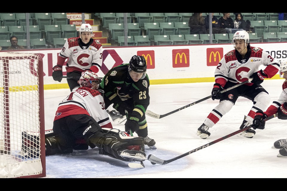 Cougars goalie Josh Ravensbergen kicks the puck off the stick of Raiders forward Harrison Lodewyk during Saturdays 5-4 home win at CN Centre.