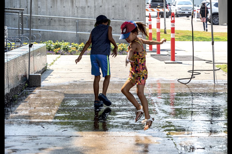 Sage Pighin leaps out of the misting tent as her brother Landon, 8, runs back into the cooling water while enjoying their time at Downtown Summerfest at Veterans Plaza in front of City Hall Saturday.