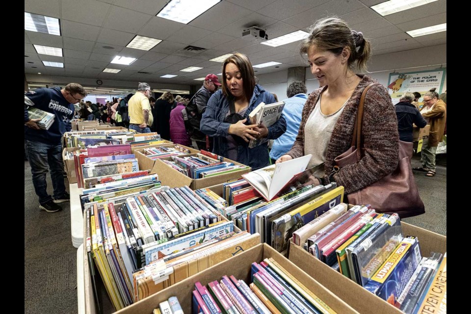 Amanda Desrochers (left) and Jaqueline Pereira chat as they search for goodies among the 165 boxes of books that went on sale to Friends of the Library members Friday at the Bob Harkins Branch. The sale continues on Saturday from 10 a.m.- 2:30 p.m. for all members of the public with books available for a cash donation.