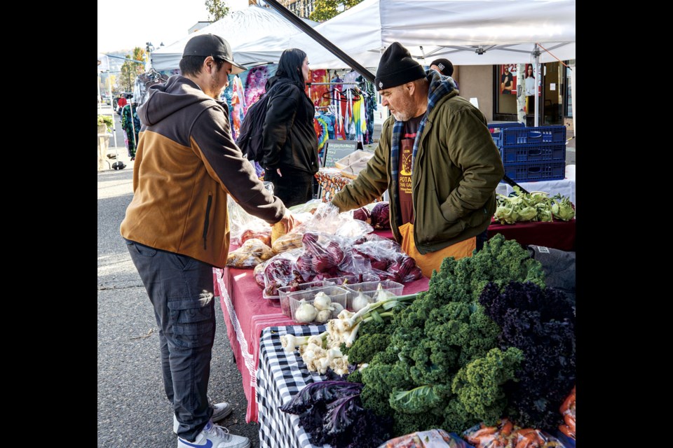 Mike Proulx and his father Leon arrange produce on the table of the booth for Leon and Sakhon Thai Garden at Saturday's Farmer's Market at Third Avenue and Quebec Street.