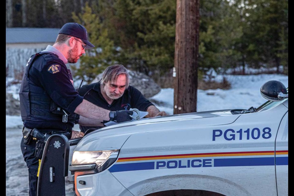 An RCMP officer reads paperwork to a man prior to releasing him after he was detained during the course of a raid on a home at 4102 First Avenue Monday, Feb 23, 2025 in Prince George, BC.