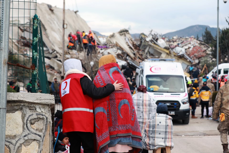 A Syrian Arab Red Crescent relief worker comforts a woman watching rescuers search through the rubble in Syria after last week's devastating earthquakes.