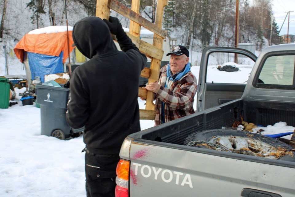 George Rowe, right, helps a Moccasin Flats resident carry a load of pallets to his campfire Thursday morning. Lowe has been taking firewood to the camp for nearly two months.