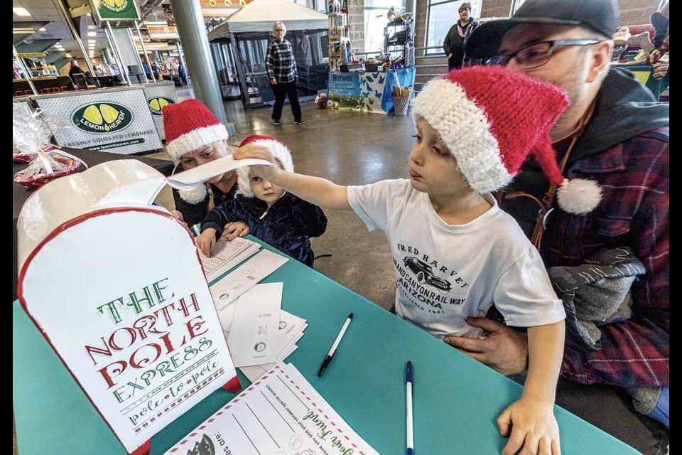 Luke Palmer, 3, puts the letter to Santa he wrote, with a little help from dad Giles, into the special mailbox at the Live Well Prince George Society booth as sister Annelise, 2, and mom Heidi work on a special letter Sunday at the Jingle Bell Christmas Craft Fair.