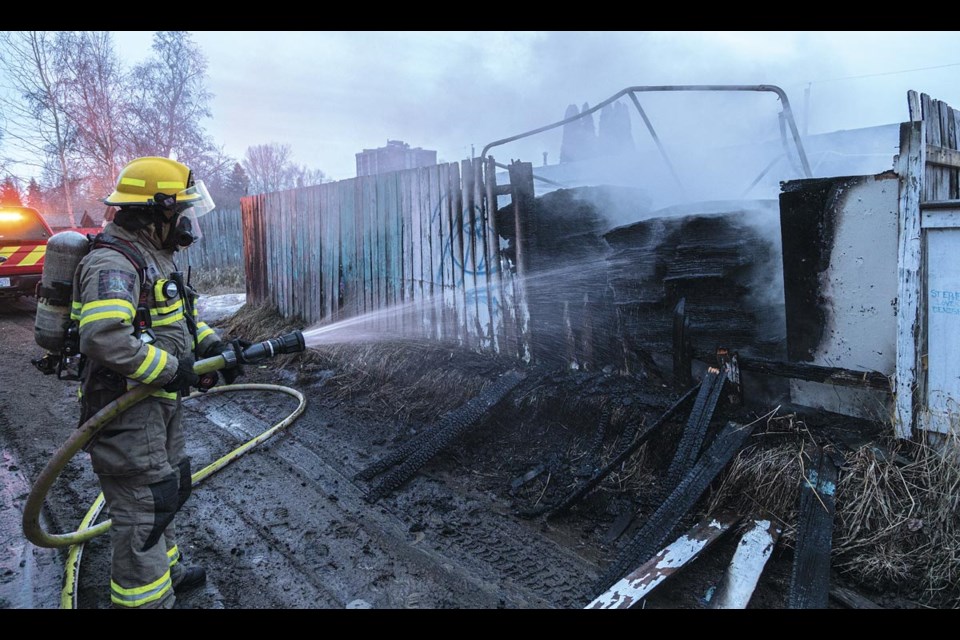 A firefighter sprays a stack of shingles in the backyard of a house in the 2100 block of Oak Street early Friday, March 21, 2025. The fire, which started about 6:45 am, consumed a stack of shingles and the fence into the back alley. There did not appear to be any injuries.