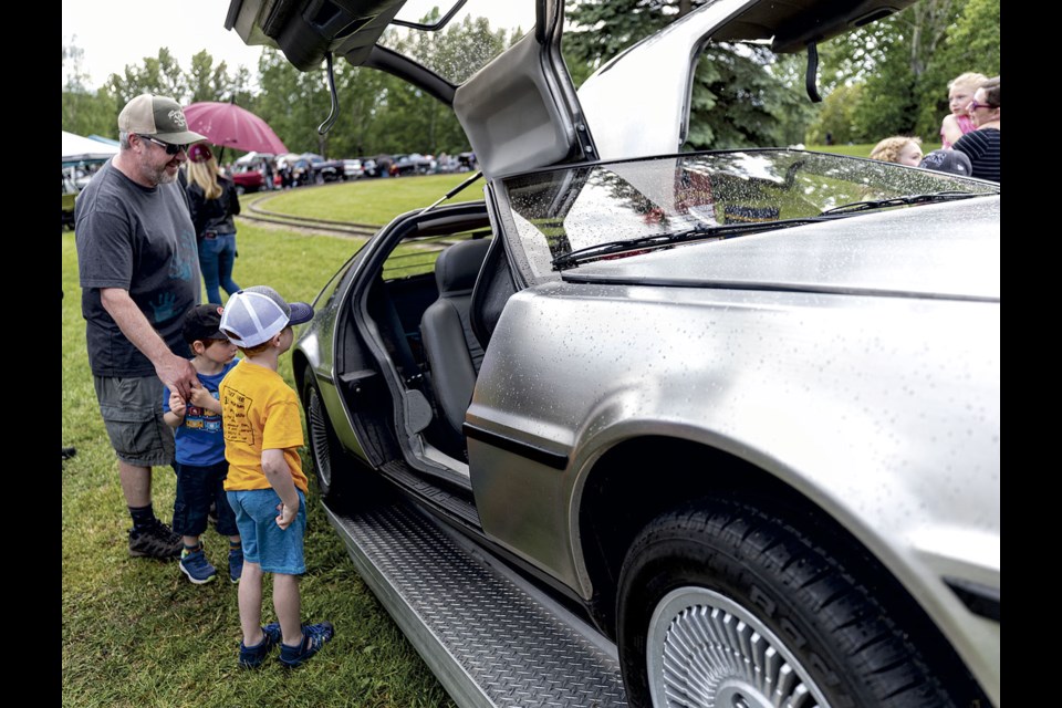 Eric Paulson explains the significance of a gleaming, though beaded with rain, stainless steel Delorean to his sons Lukas, 6, and Jesse, 3,  as they take in the cars on display for the annual Cruisin' Classics Father's Day Show and Shine Sunday at Lheidli T'enneh Memorial Park.