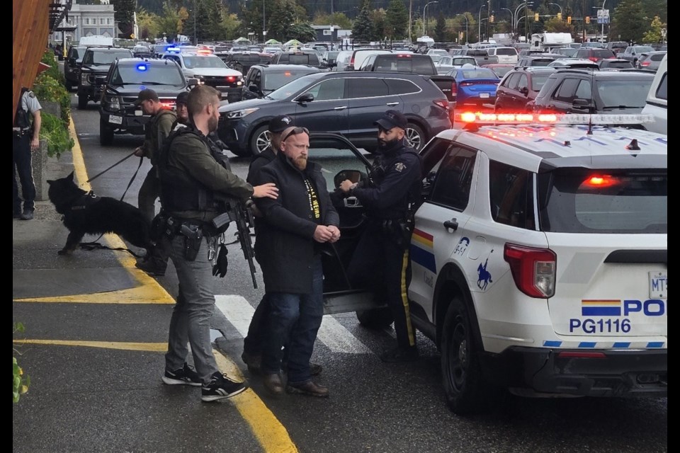 A man is led out of the CIBC branch at Spruceland Mall on Wednesday, Oct. 2, 2024 in Prince George, BC. A police dog can be seen heading into the building at left. RCMP maintained a heavy presence at the plaza after an incident around the noon hour.