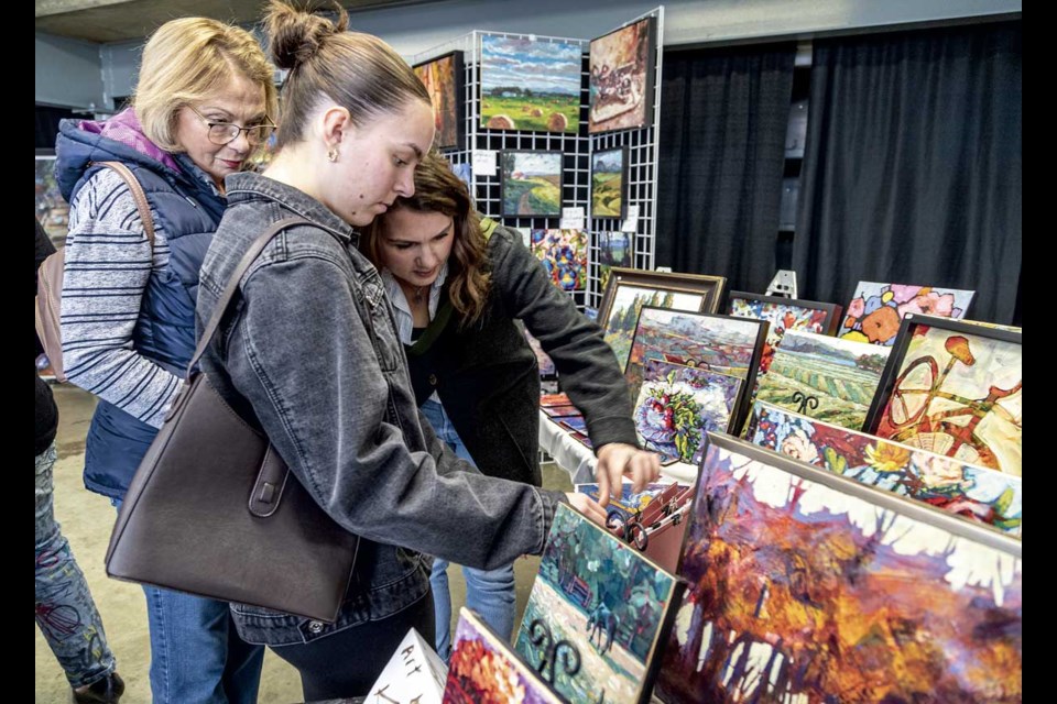 Cathy McDonald (back), Remi Patterson and Nicole Fraser (bending) look at a selection of artist Karma Vance's paintings Saturday at the Federation of Canadian Artists Central Interior Chapter booth at Studio Fair held in CN Centre this weekend.