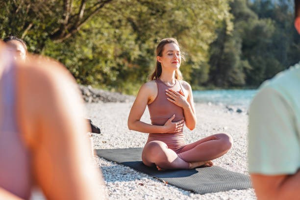 Group of people enjoying a peaceful yoga practice in nature near a river on a sunny morning