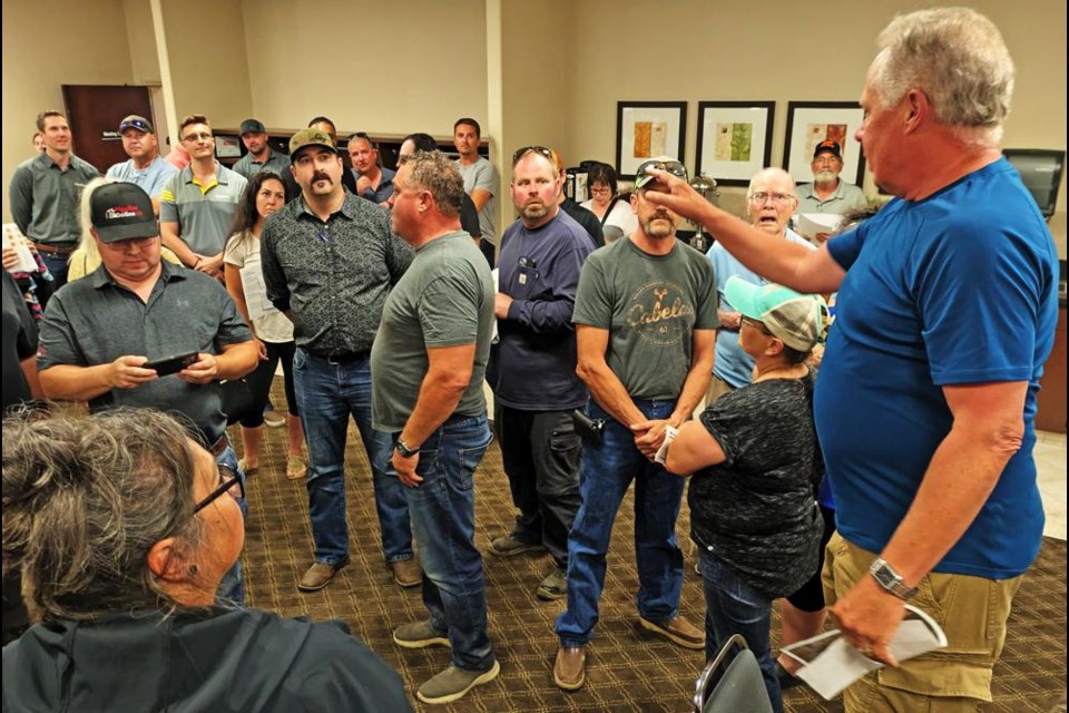 Kim Brady, standing on a chair at right, called for the packed room to be quiet so they could field questions to Enbridge representatives, at the open house the company hosted at the Ramada Hotel on July 17 in Weyburn. Brady will moderate the public meeting set for July 31 at McKenna Hall.