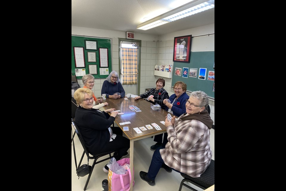 A group of ladies gather for a game of cards, with photos in the background that were submitted for the district games.