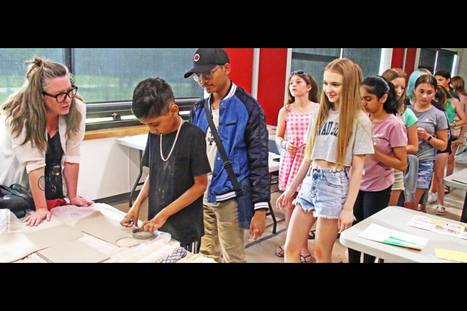 Instructor Regan Lanning helped Aarav Sharma, Tim Portugal and Olena Shved make bottoms for their clay mug projects on July 10.