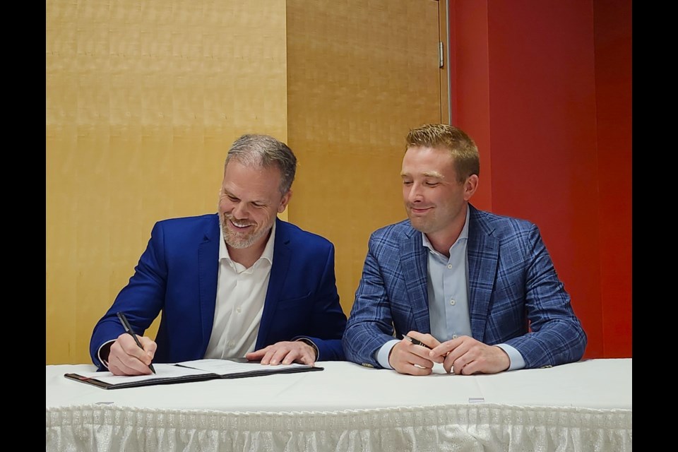 Federal Health Minister Mark Holland, left, signs the agreement while his provincial counterpart, Jeremy Cockrill, looks on.