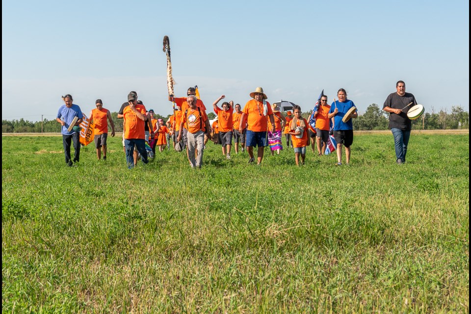 Walkers walk across the field near where the Residential School stood in Delmas.