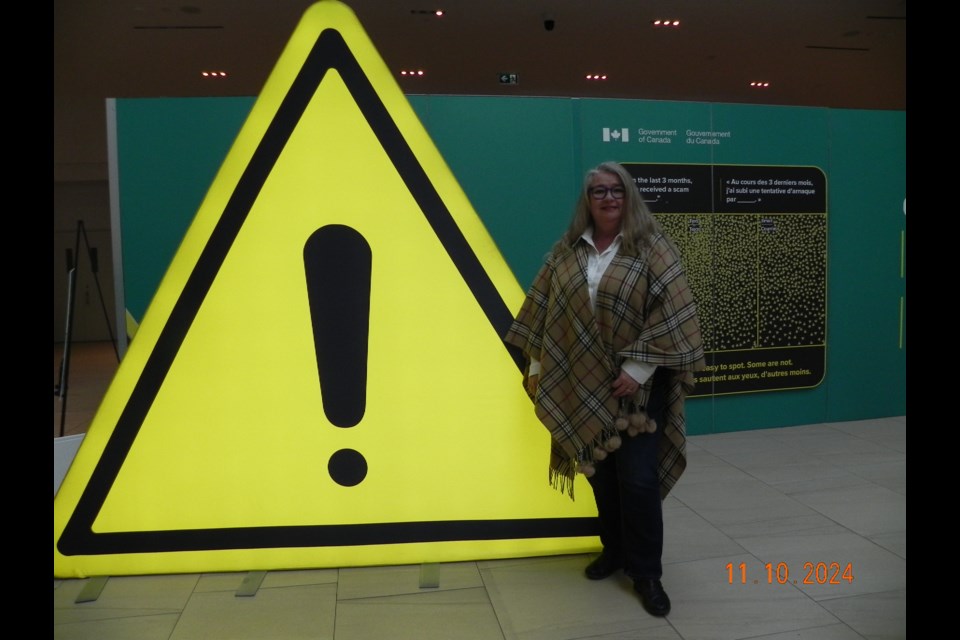 Joanne de Waal, Communications Manager, from Moose Jaw CRA office, stands by attention-grabbing caution sign, part of the escape room experience offered to the public with intention of educating residents on spotting scams.                      