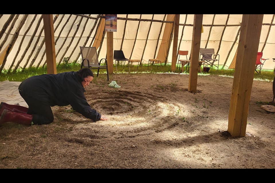 Aerial Sunday-Cardinal from Whitefish Lake First Nation in northern Alberta, shaping seven circles out of sand representing different generations before rising and singing the Grandmother Song.