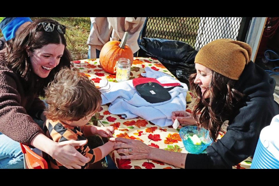 Weyburn Co-operative Playschool teacher Luanne Akins held a rub-on tattoo on Milo's wrist, encouraged by his mom Shelby, at one of the booths for the "Pumpkin Patch" held Saturday afternoon at Jubilee Park.