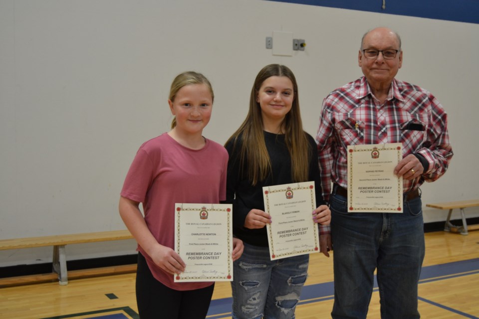 Preeceville School students who were presented prizes for their winning entries in the Remembrance Day contest, from left, were: junior black and white poster category, Charlotte Newton and Blakely Firman (junior black and white poster winners) and Blaine Medlang, Legion poppy chairman.