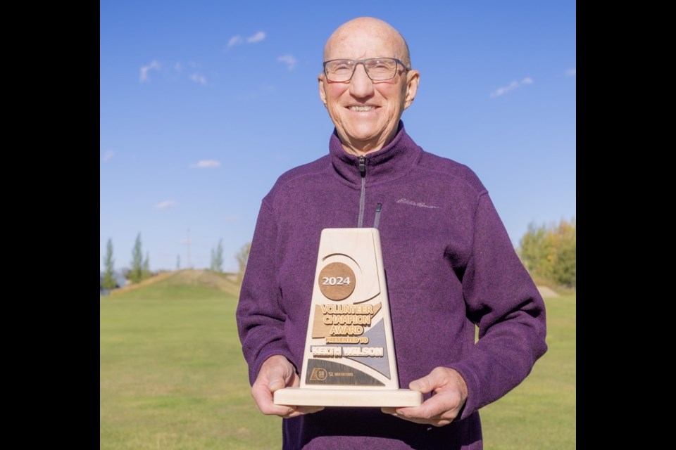 Keith Wilson stands in front of Wilson Hill, a beloved toboggan hill named after him, with the first ever Volunteer Champion Award.