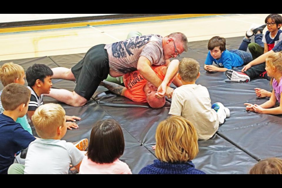 Wrestling coach Ken Kot, and substitute teacher Kevin Butz, demonstrate a basic wrestling move to a Grade 3 class before having them try it on Wednesday.