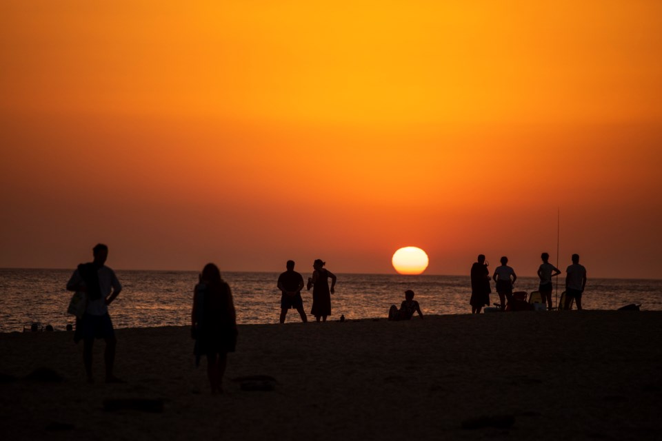 FILE - People watch the sunset sitting on a beach next to the Trafalgar Lighthouse in Los Caños de Meca, Spain, on, July 29, 2020. (AP Photo/Emilio Morenatti, File)