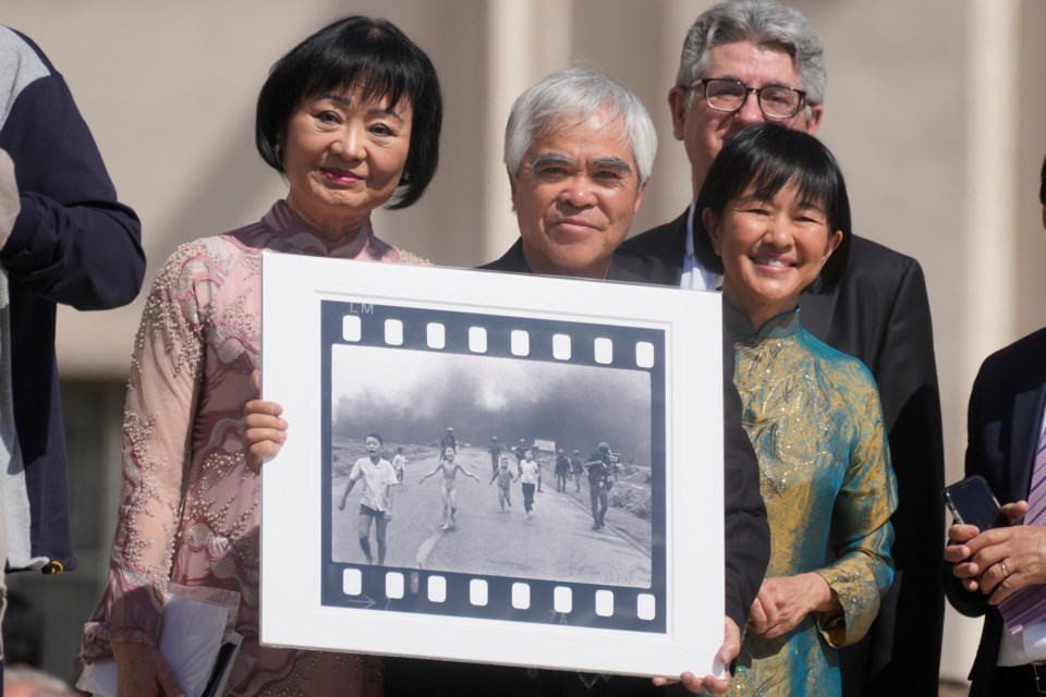 FILE - Pulitzer Prize-winning photographer Nick Ut, center, flanked by Kim Phuc, left, holds the "Napalm Girl", his Pulitzer Prize winning photo, as they wait to meet with Pope Francis during the weekly general audience in St. Peter's Square at The Vatican, Wednesday, May 11, 2022. (AP Photo/Gregorio Borgia, FILE)